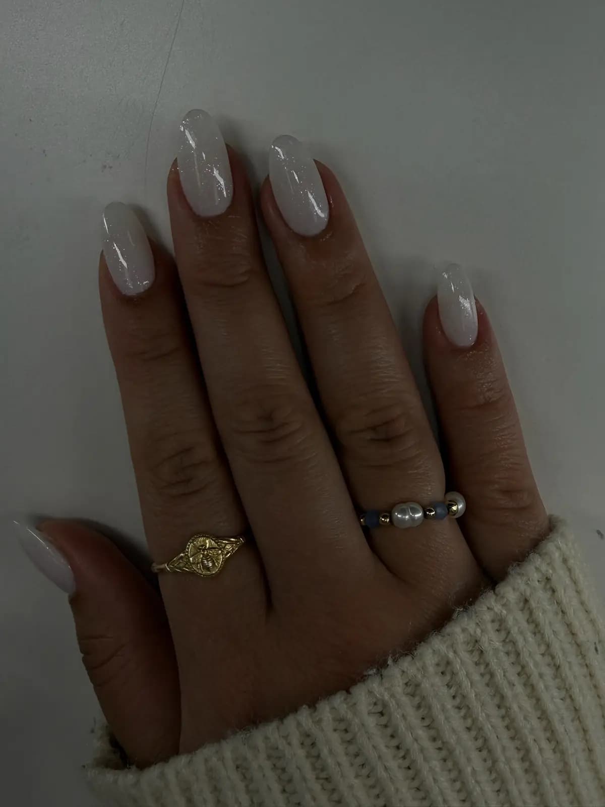 Milky nude gel manicure on medium almond nails, with thin gold rings