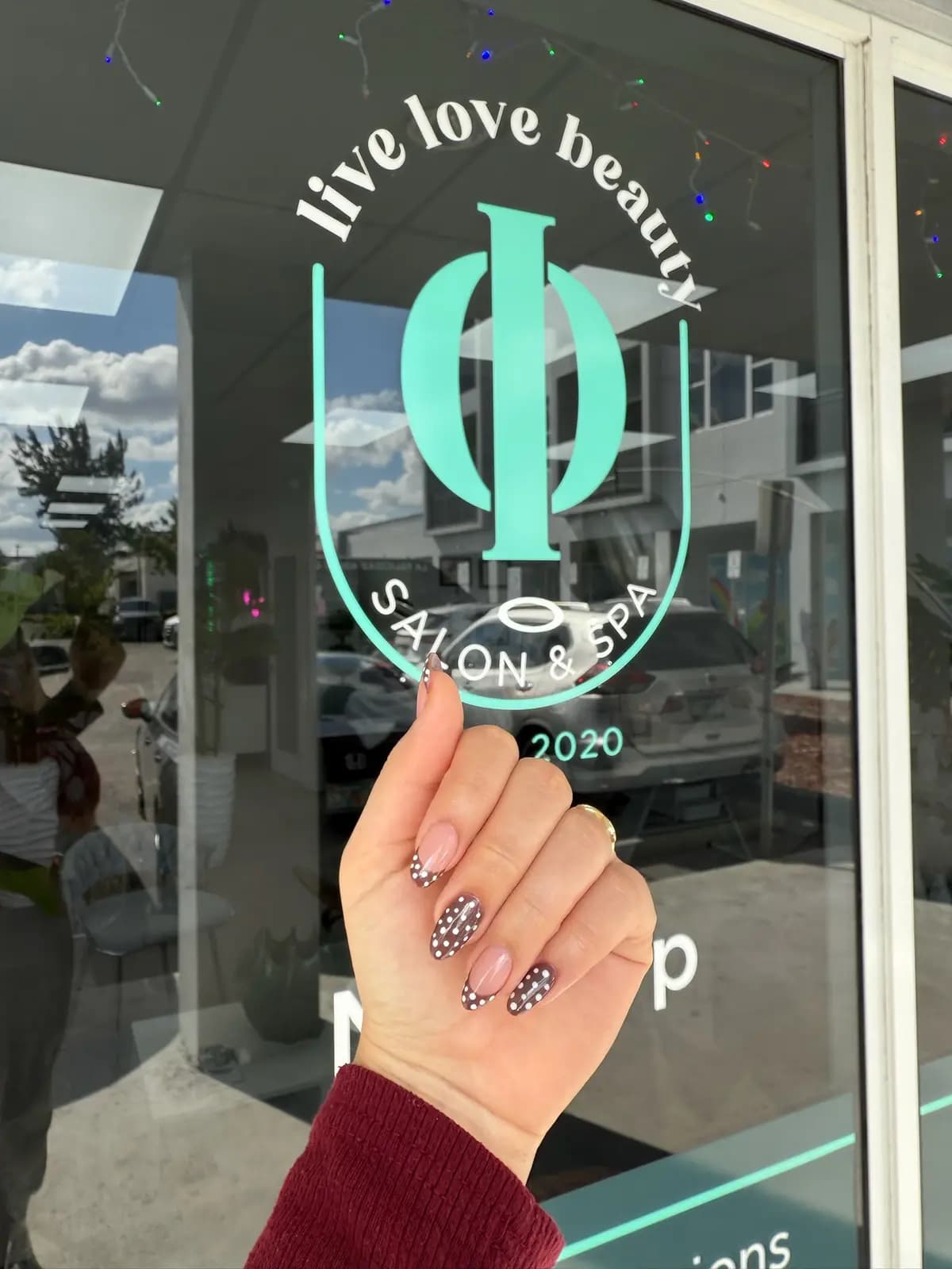 Hand with nail art in front of the Live Love Beauty Salon & Spa window