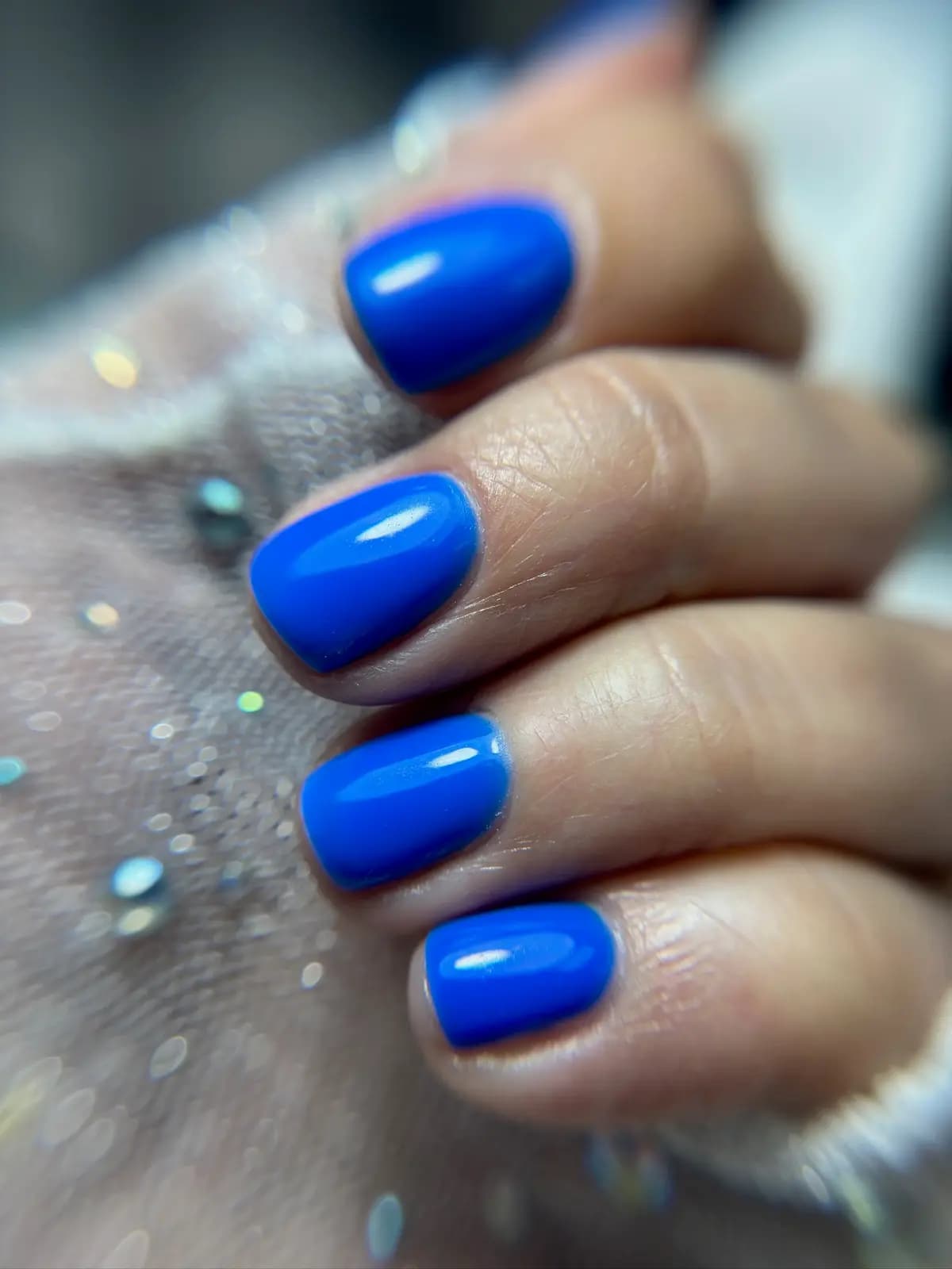 Glossy cobalt blue gel nails on the work table with loose glitter