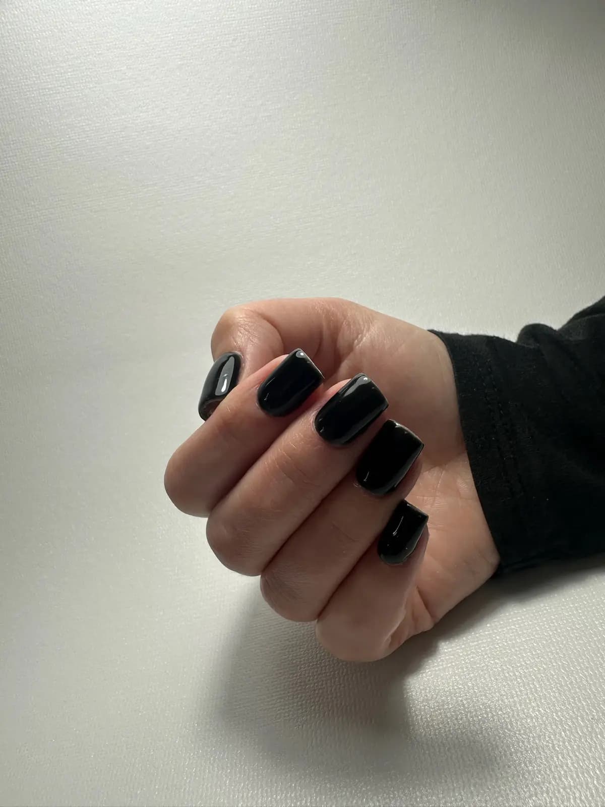 Black gel manicure on short nails, closed hand on a light background