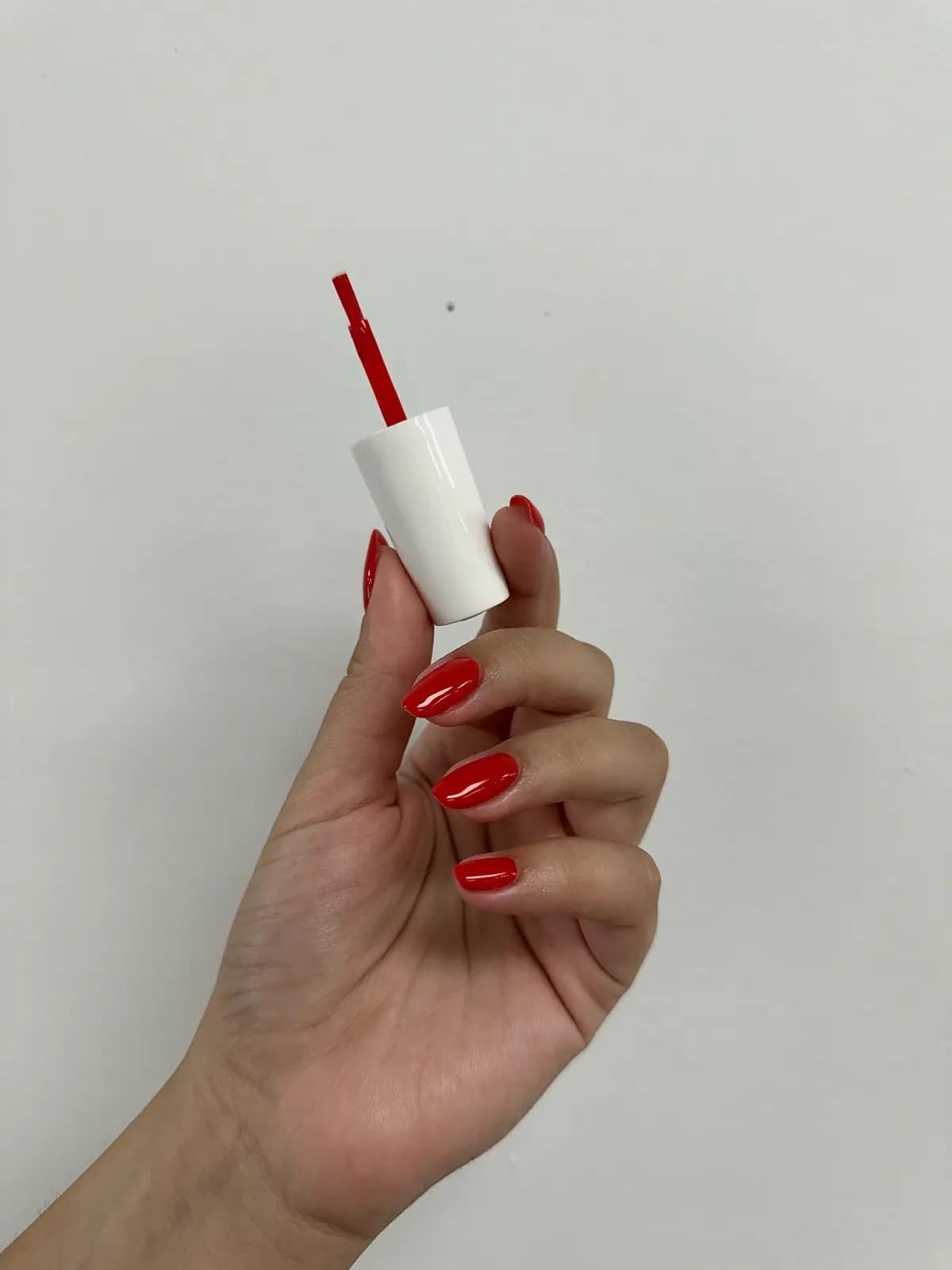 Hand with red nails holding a bottle of red polish