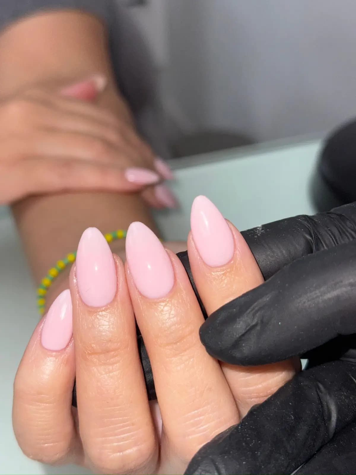 Pale pink gel almond nails held by the technician in black gloves