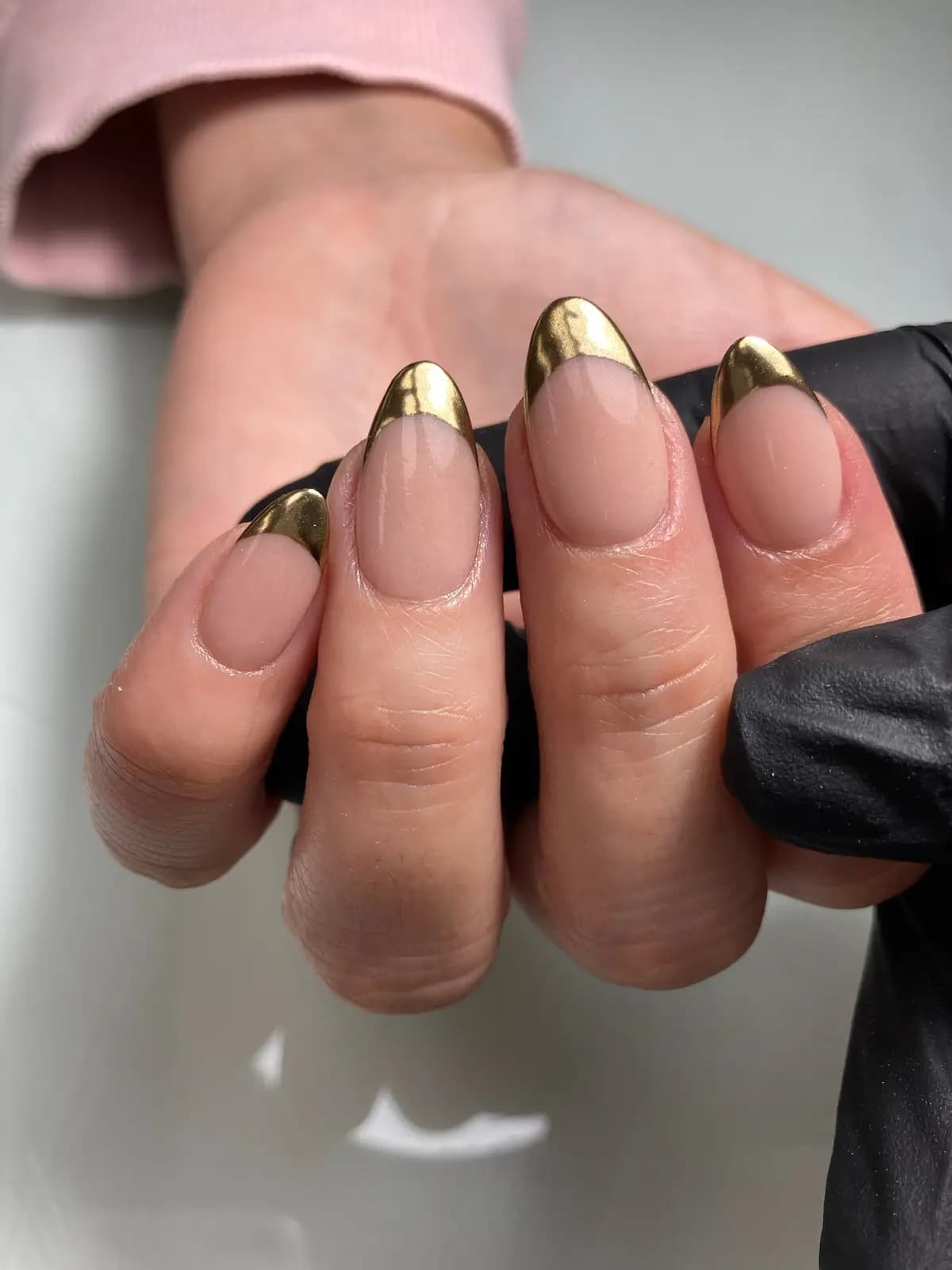 Gold chrome tips over a nude base on almond nails