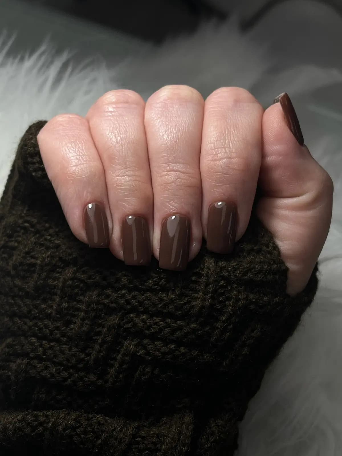 Short nails in chocolate brown gel over a knit sweater