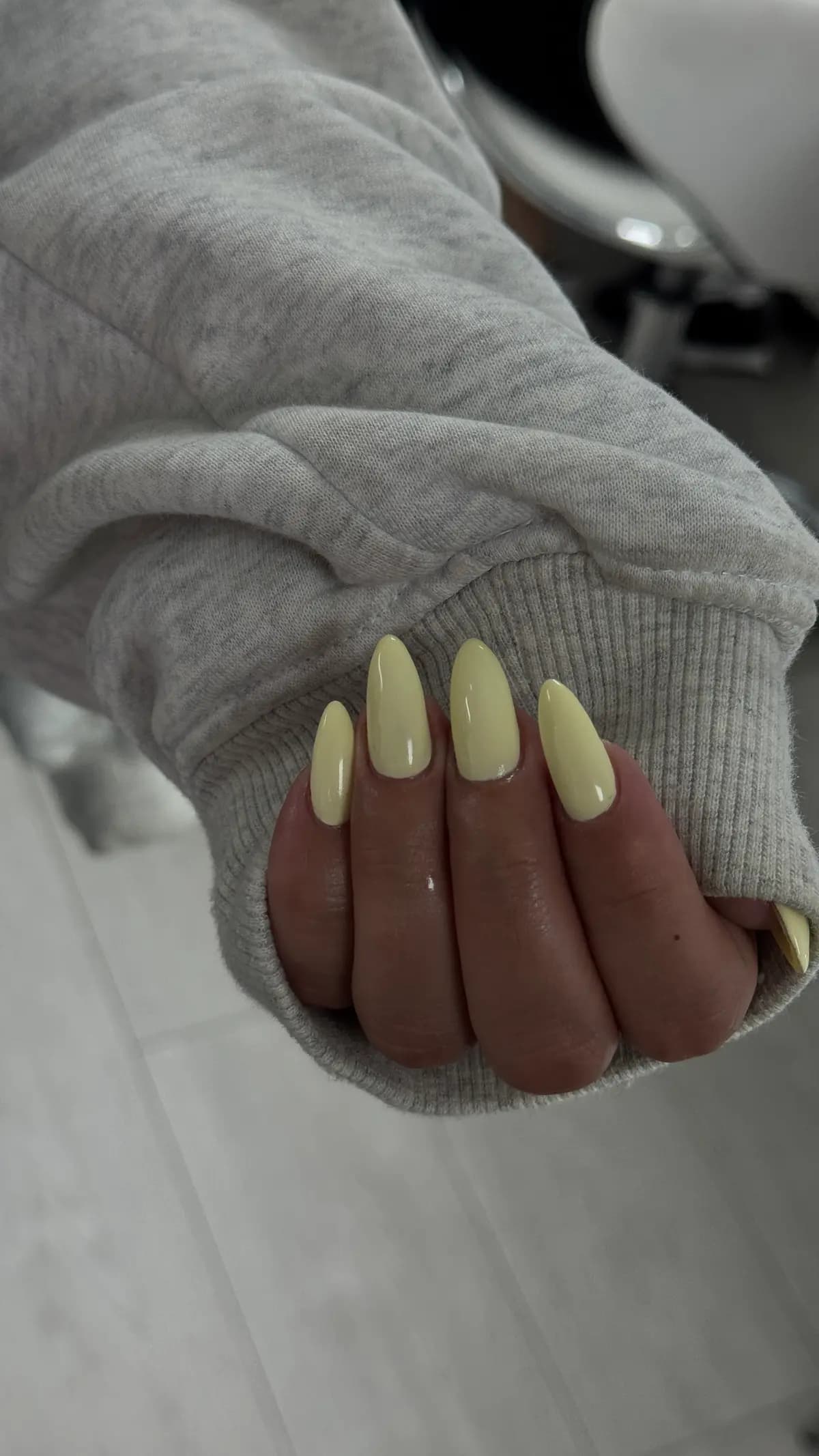 Long almond nails in pale yellow gel, hand on a grey sweatshirt