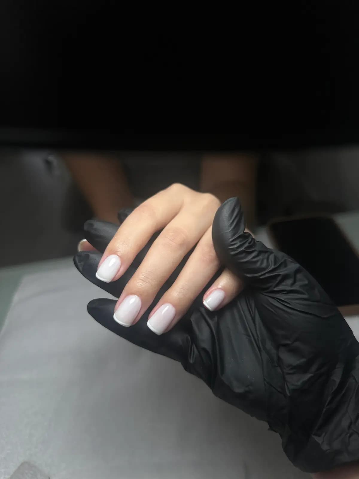 Short square nails in milky white gel held in a black glove