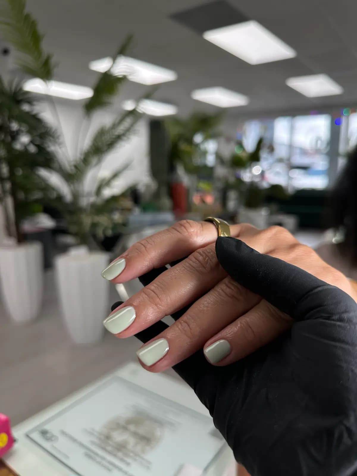 Pearl white nails finished inside the salon, plants and floor behind
