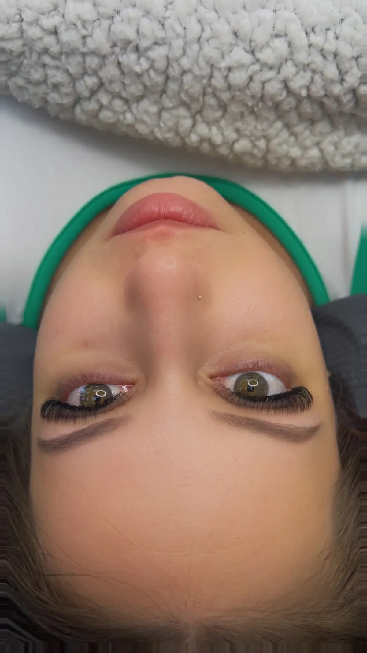 Client reclined on the bed with a green headband, lash extensions on and brows shaped