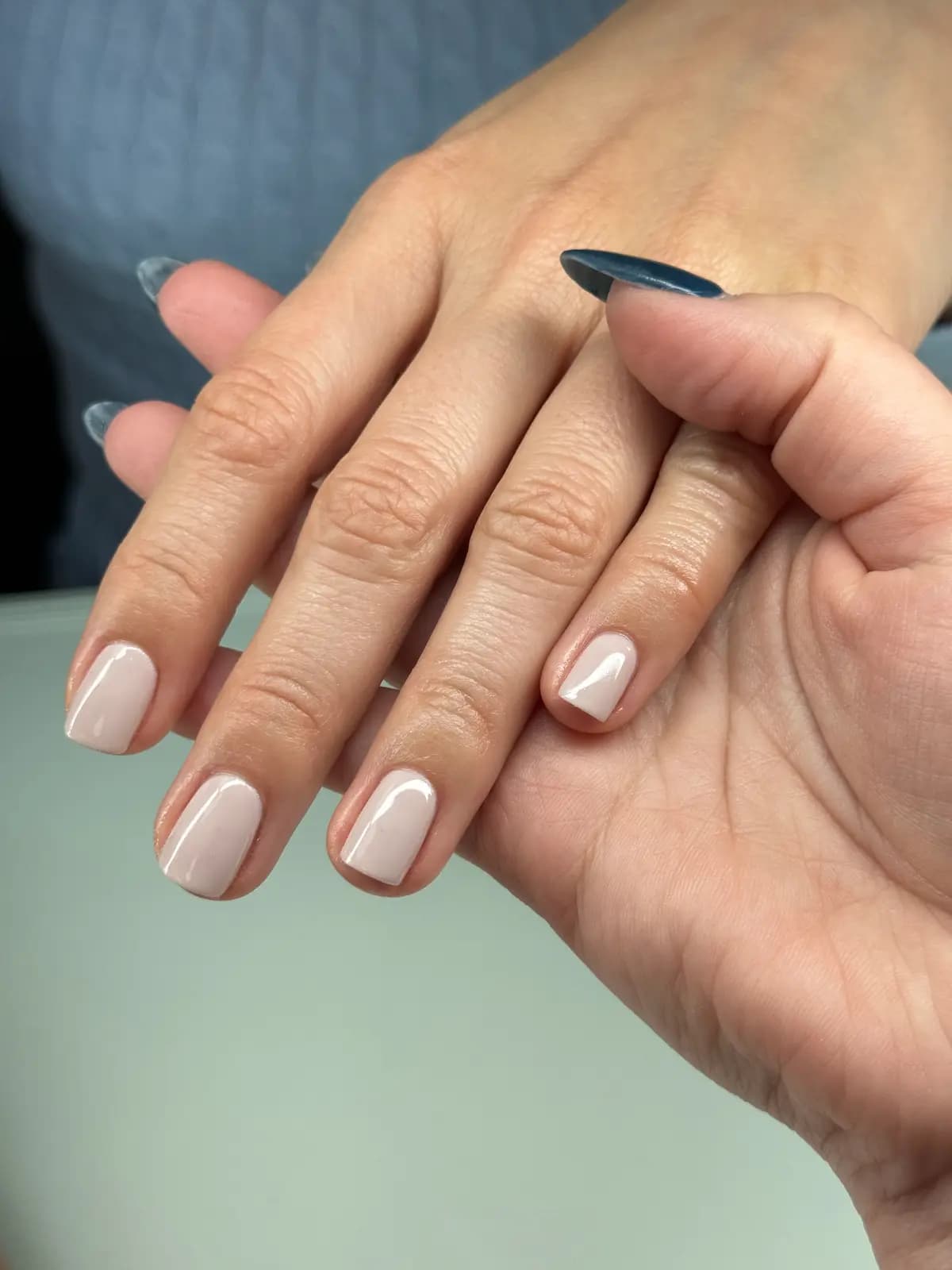 Short off-white nude nails, both hands on the table