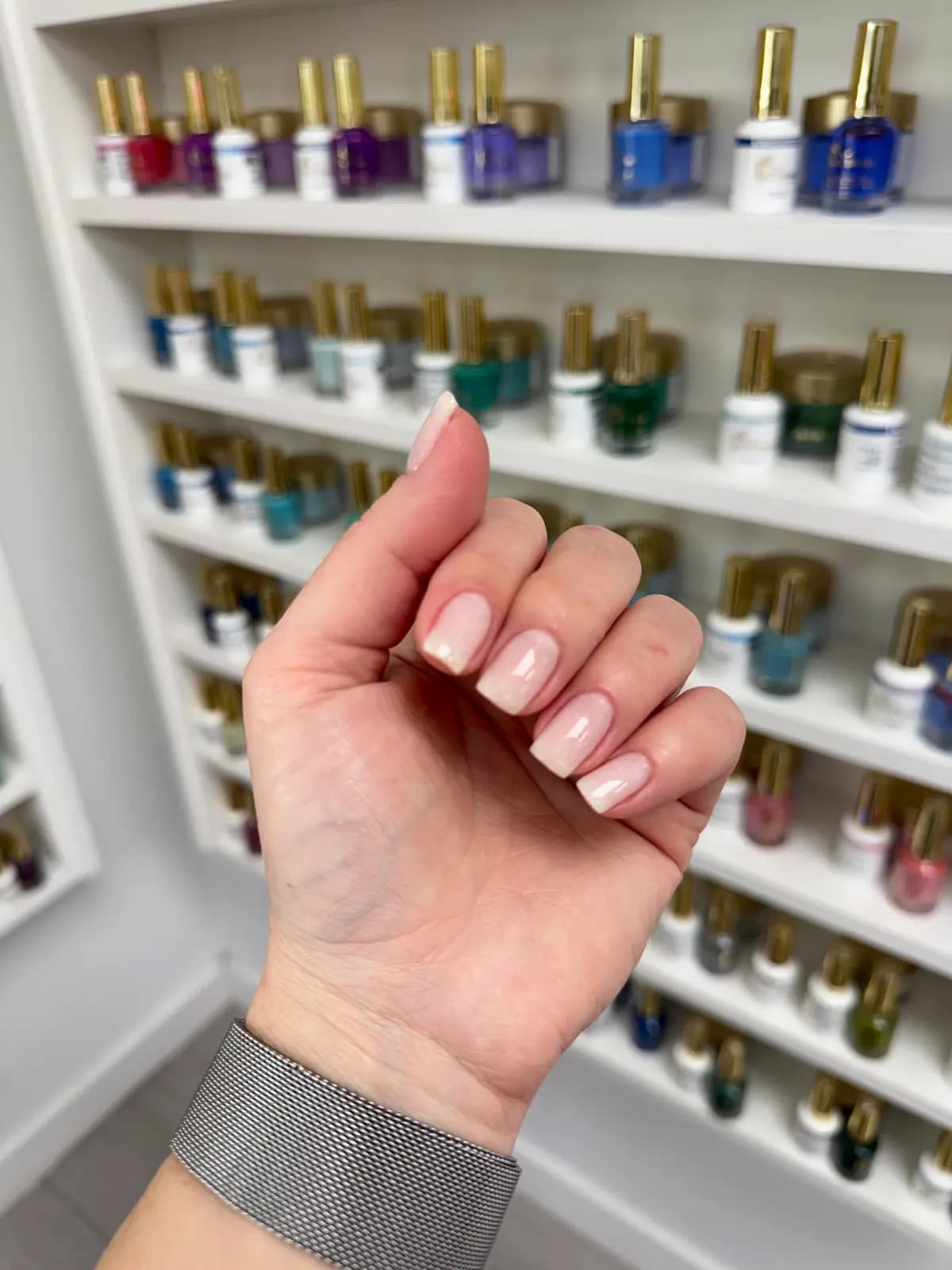 Natural-length nude nails in front of the salon's polish wall