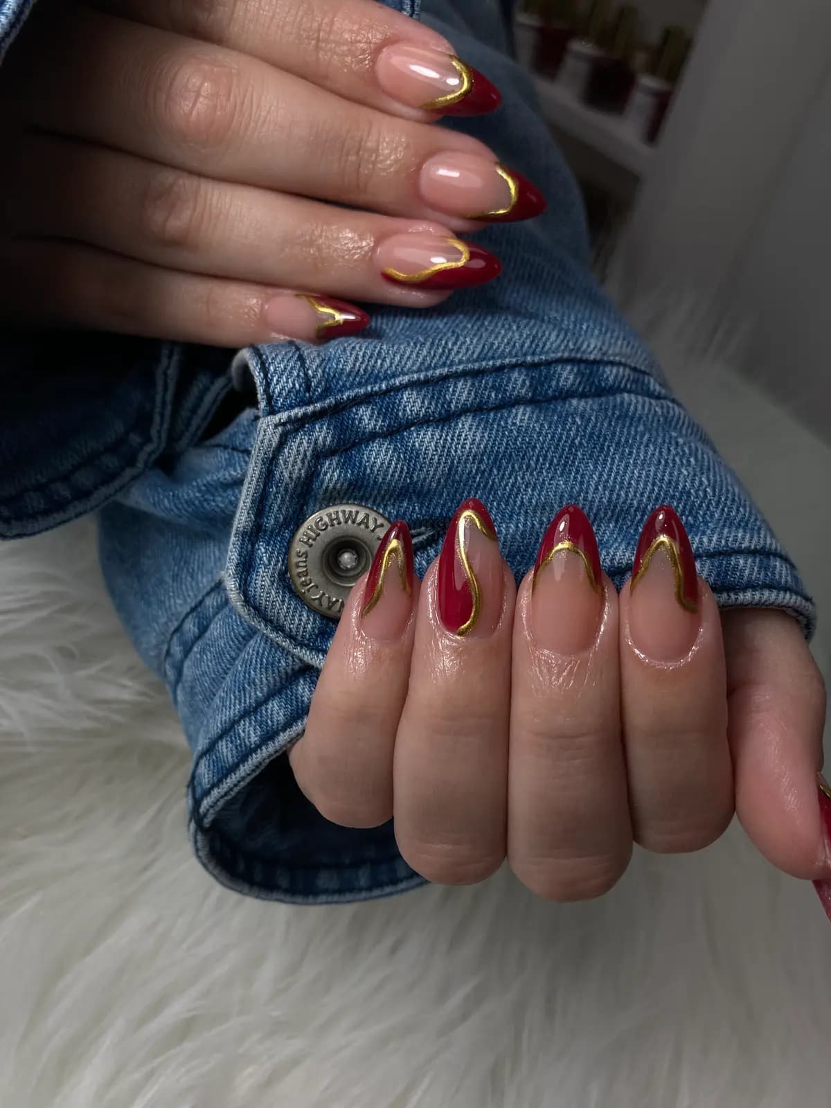 Red stiletto nails with gold chrome french, against denim