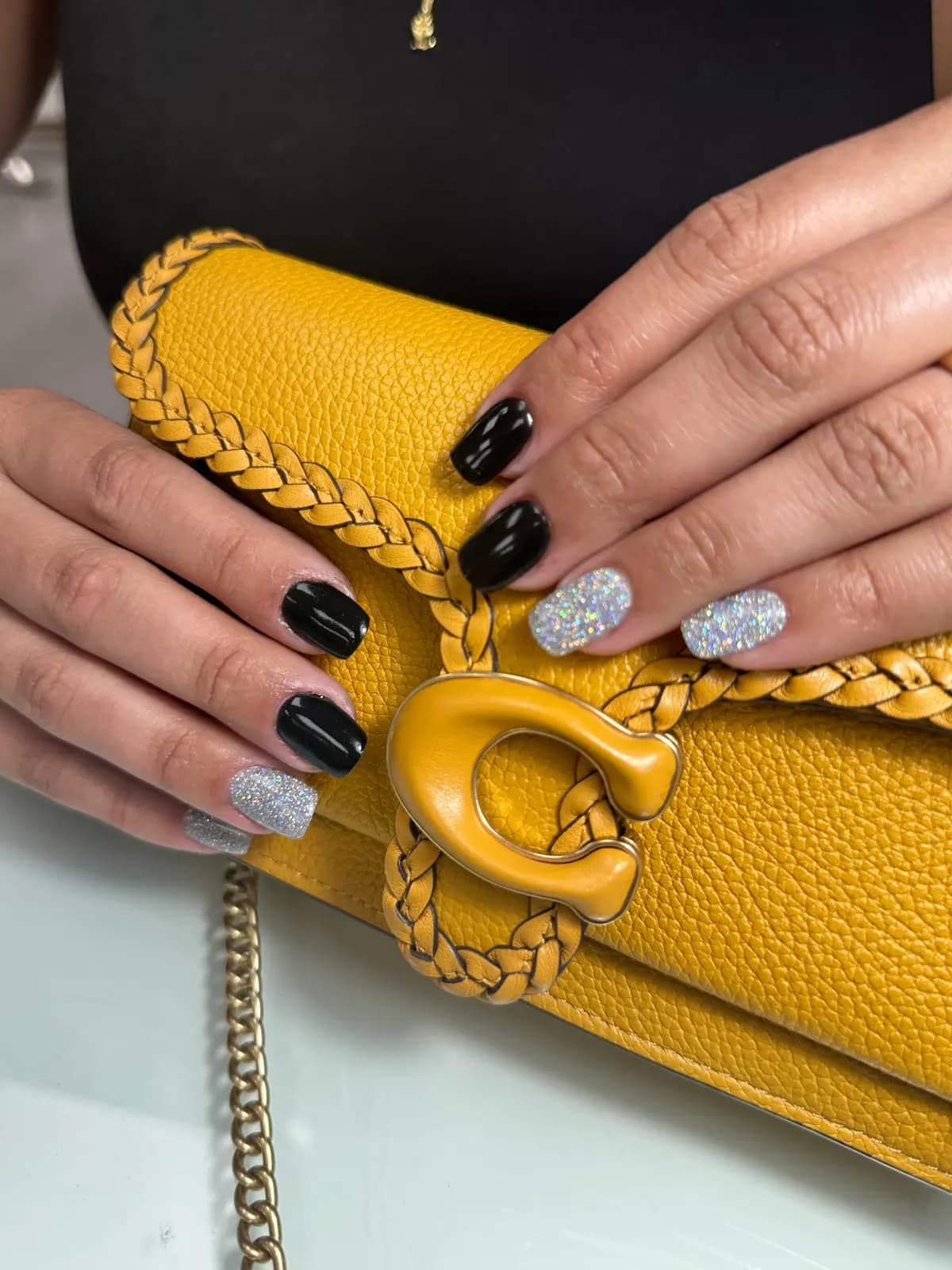 Black nails with silver glitter accents, next to a yellow bag