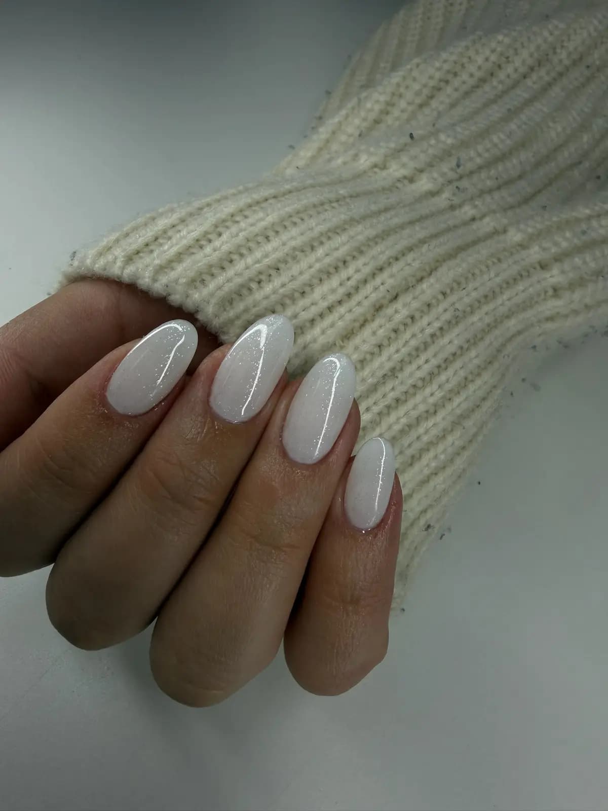 Pearl white gel manicure on almond nails, against a cream knit sweater