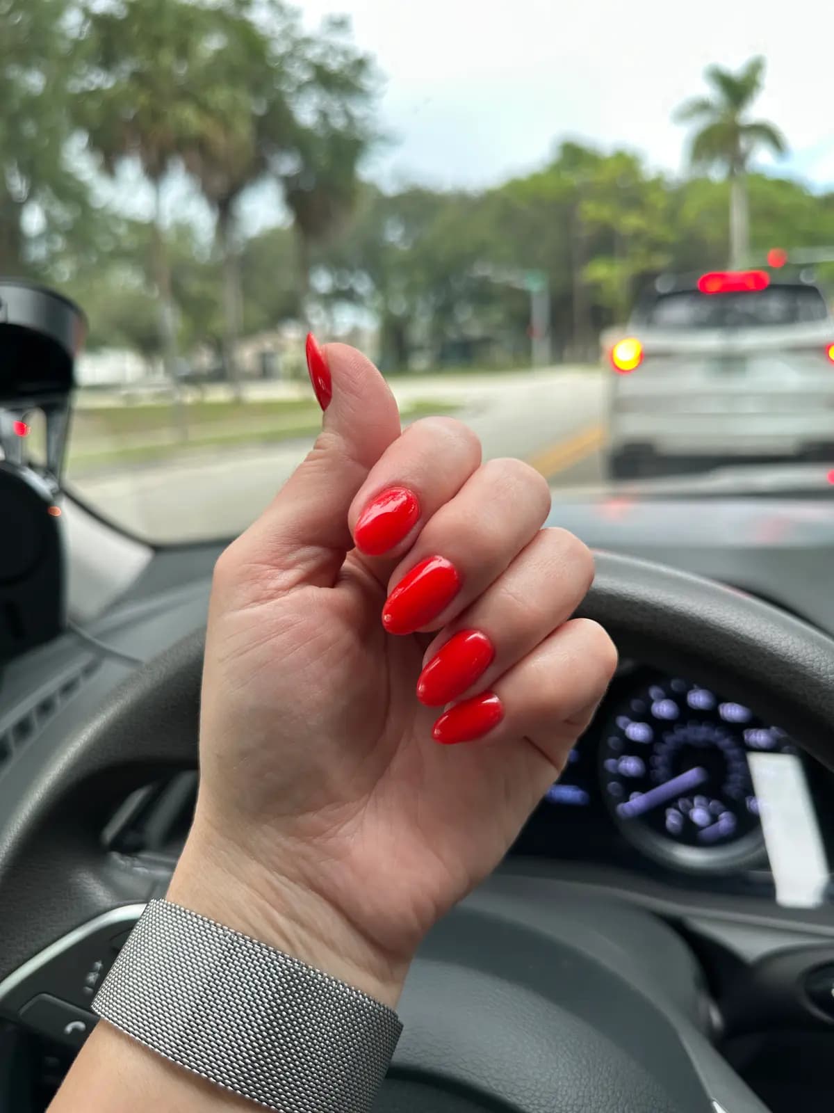 Bright red gel almond nails, hand on the steering wheel