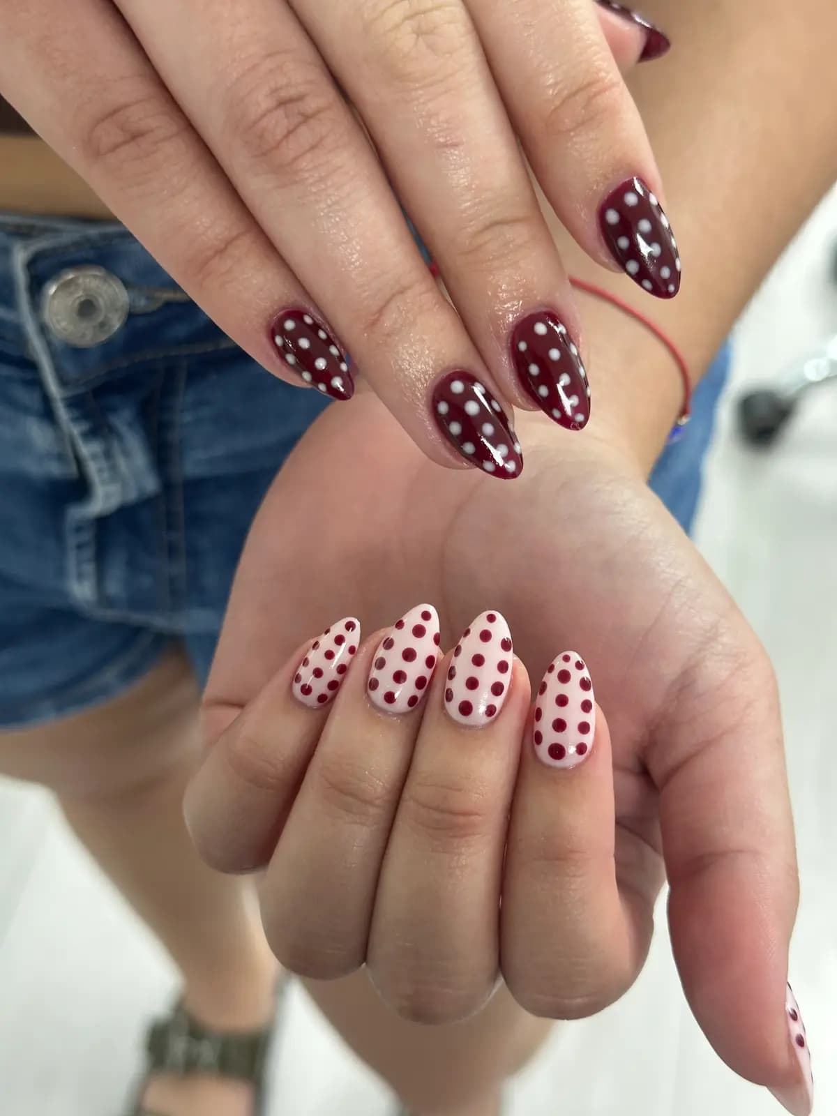Long nails with burgundy polka dots over alternating pink and burgundy