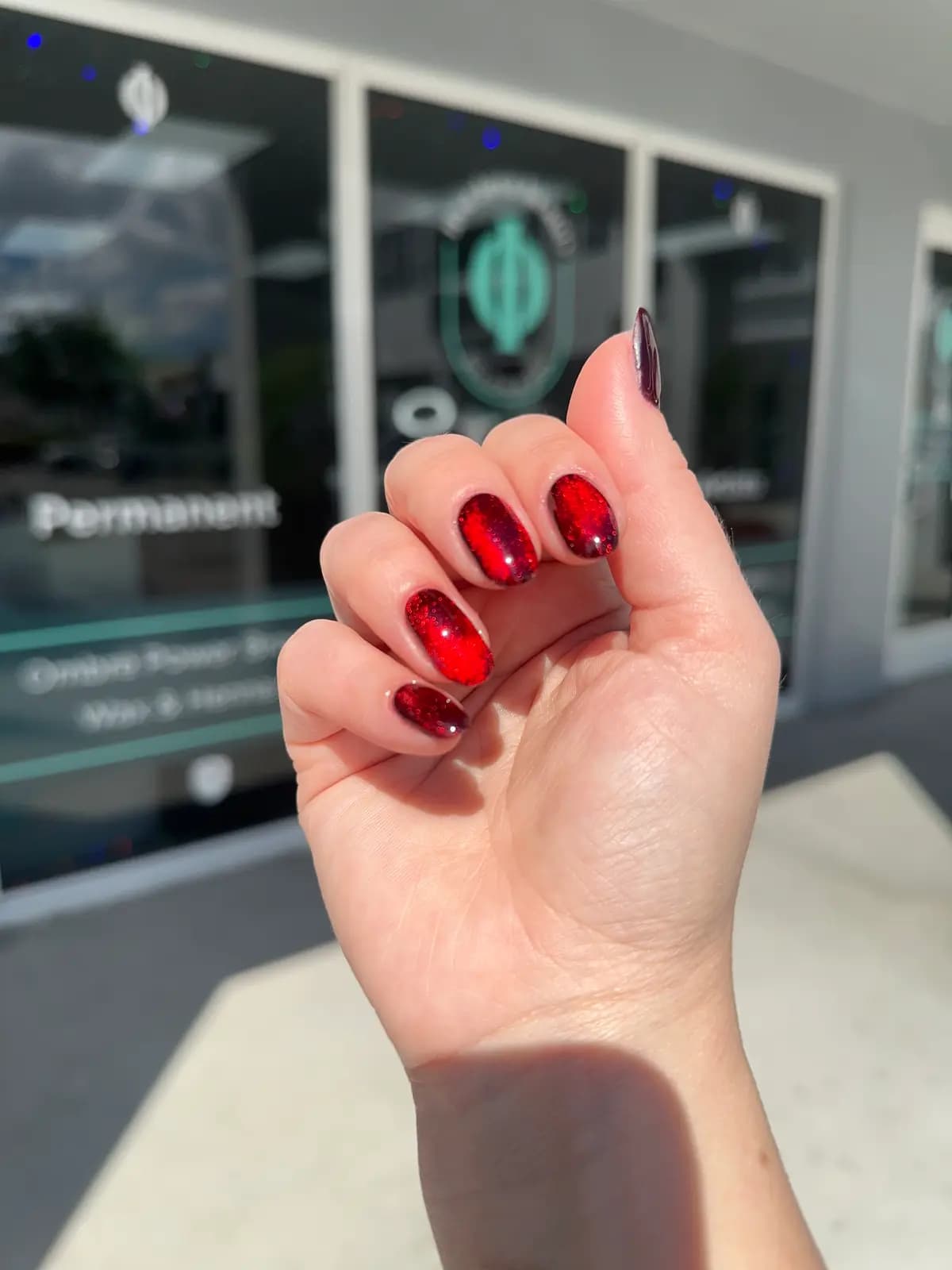 Short red gel nails, closed hand in front of the salon window