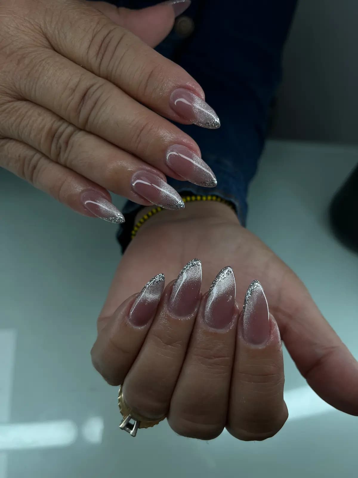 Silver glitter tips over a nude base on almond nails