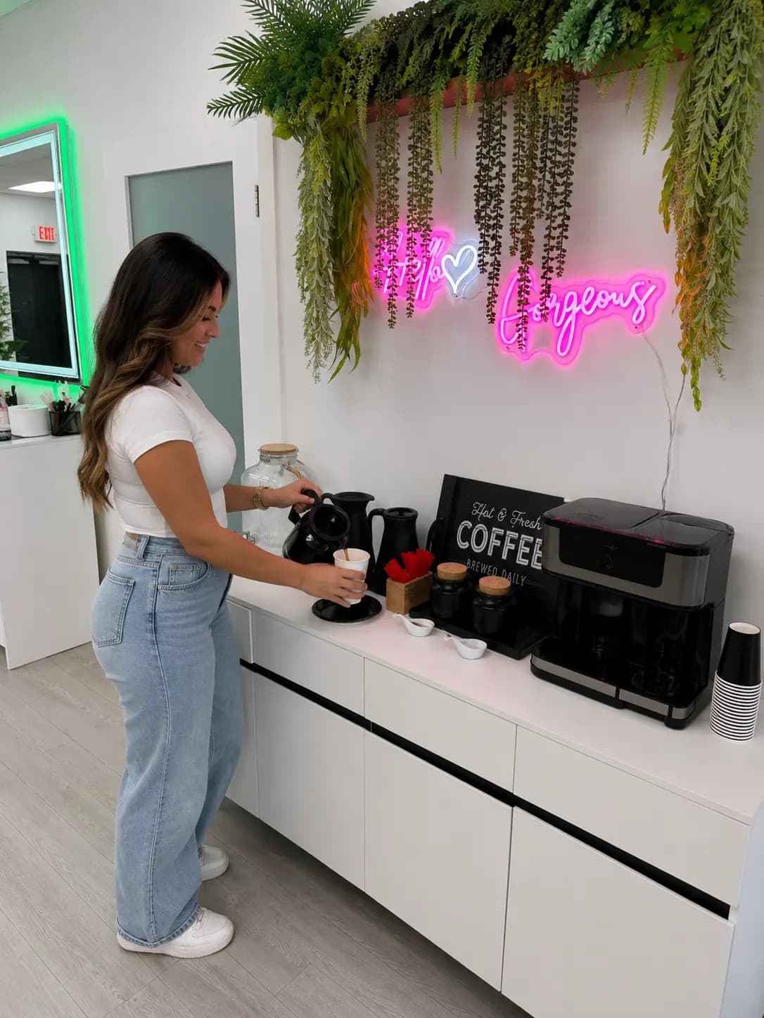 The salon coffee station under the "Hey gorgeous" neon, with hanging plants