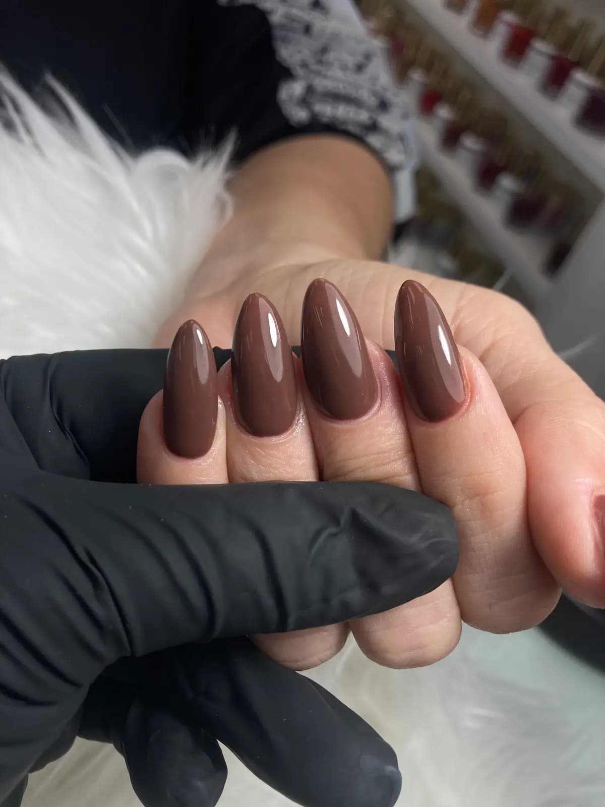 Cocoa brown gel almond nails held in a black glove