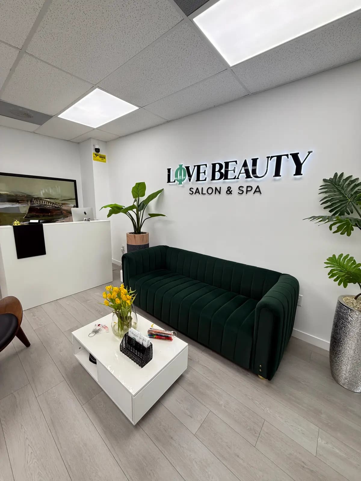 Reception at Live Love Beauty Salon & Spa in Hialeah: backlit sign, green velvet sofa and white front desk